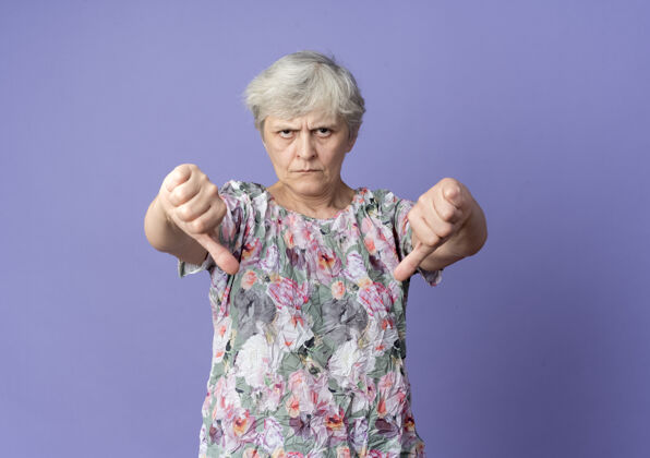 二严肃的老妇人竖起大拇指 两只手孤立在紫色的墙上手拇指老