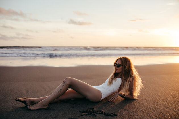 美丽迷人的白种女人戴着时髦的耳环在沙滩上摆姿势度假成人日落太阳