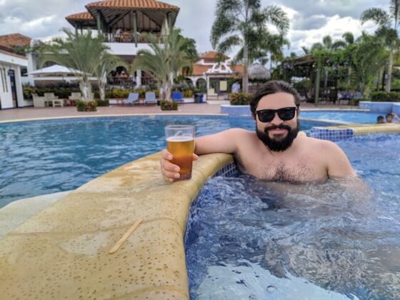 举行一个长着胡子的帅哥在游泳池里拿着一杯啤酒太阳镜放松水