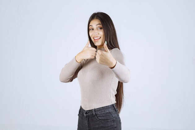 雇员穿灰色衬衫的女孩在做竖起拇指的招牌员工年轻享受