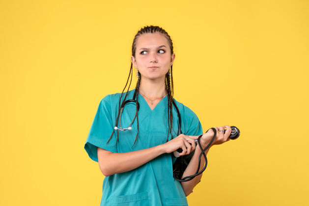 前面身穿医疗服的女医生在黄色墙壁上检查压力的正视图听诊器女医生人