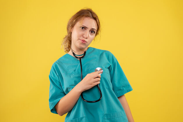 病毒黄色墙壁上穿着带听诊器的医疗服的女医生的正视图前台听诊器女医生
