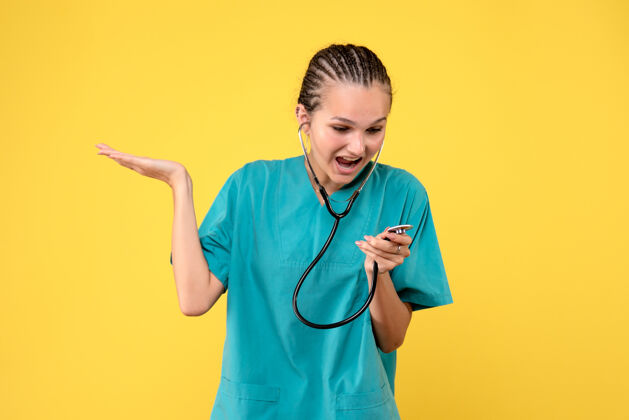 健康黄色墙上穿着带听诊器的医疗服的女医生的正视图前台医院护士