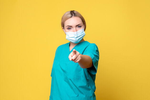 流行黄墙上年轻女医生穿着医用衬衫 戴着口罩的正面图微笑护士面具