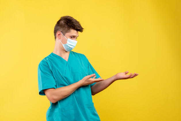 健康黄墙上带无菌口罩的男医生的前视图成人男性医生病毒