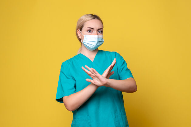 医学黄色墙壁上穿着医用衬衫和无菌口罩的年轻女医生的正面图年轻女医生流行病医院