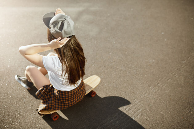 休闲在阳光明媚的城市环境中 女子滑板冠军戴着帽子坐在长板上年轻乐趣休闲