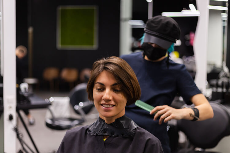 工人一个专业的女理发师给客户理发这个女孩戴着面具坐在美容院里理发师脸爆发