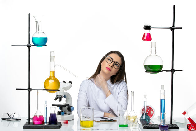 医学前视图穿着白色医疗服的女化学家坐在白色背景的科学大流行病毒冠状病毒实验室里 拿着不同的溶液人坐姿溶液