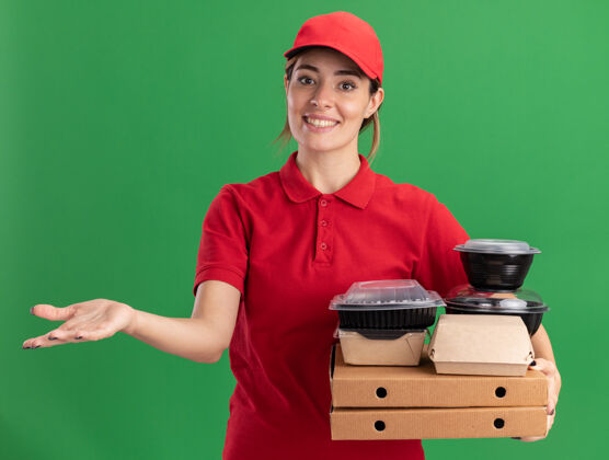成人微笑着的年轻漂亮的送货女孩穿着制服拿着纸食品包装和比萨饼盒上的容器食物披萨手