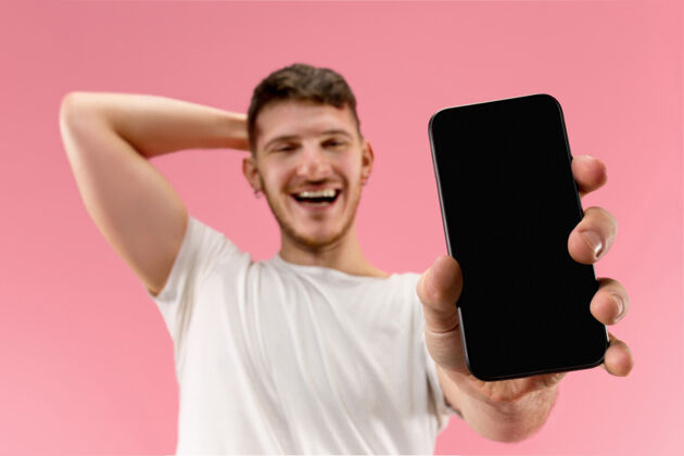 技术年轻帅哥在粉色背景下展示智能手机屏幕 惊喜万分胡须脸年轻