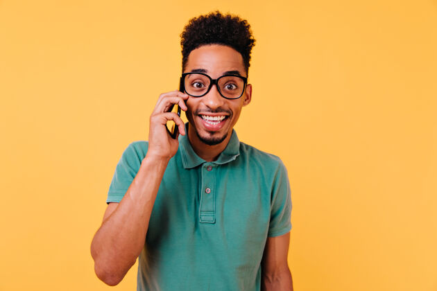 设备一个穿着时髦绿色t恤的开朗男人在打电话一个拿着智能手机微笑的无忧无虑的年轻人手机室内快乐