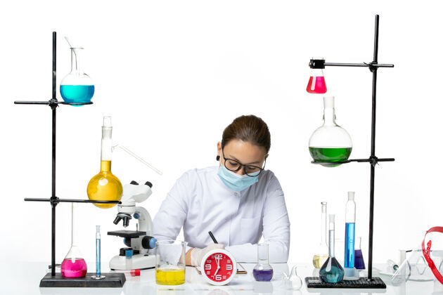 烧杯前视图穿着白色医疗服的女化学家带着面罩坐在白色背景上写着解决方案化学家实验室病毒冠状病毒-飞溅溶液化学家医学