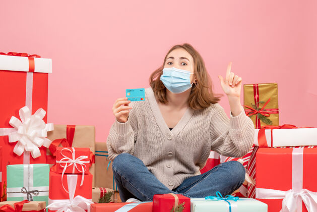 休闲正面图：年轻女性戴着面具围坐在圣诞礼物旁边病毒礼物圣诞节