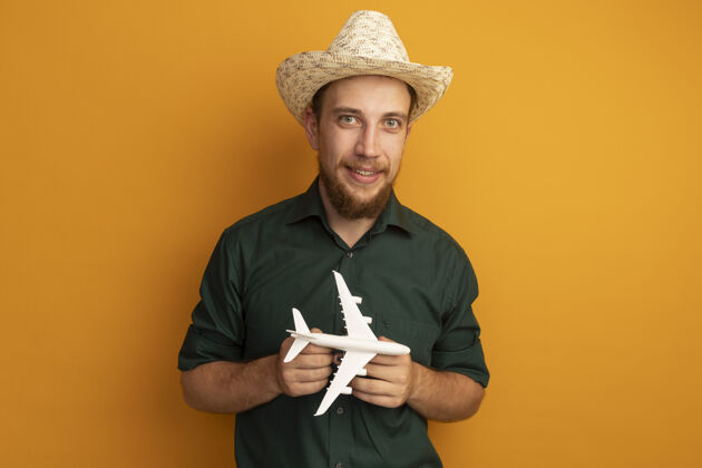 海滩笑容可掬的金发帅哥 头戴沙滩帽 手里拿着橙色的飞机模型姿势帽子黑发