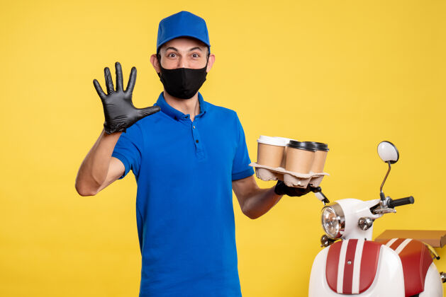 男人正面图：戴着黑色口罩的男信使拿着咖啡在黄色的工作服上工作专业面具人