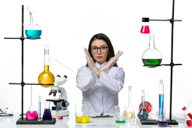 实验室前视图穿着白色医疗服的女化学家正坐着 拿着显示禁止使用白色背景科学冠状病毒大流行实验室病毒的解决方案前面玻璃病毒