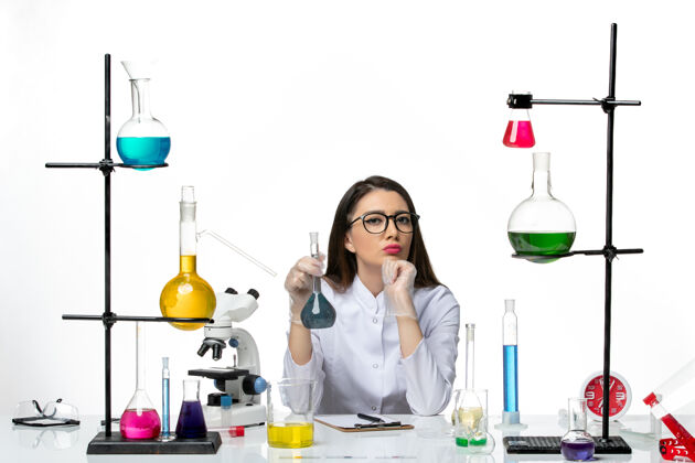 玻璃前视图穿着白色医疗服的女化学家拿着浅白色背景上蓝色溶液的烧瓶实验室科学病毒冠状病毒大流行实验室套装药品