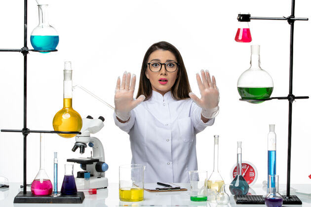 肖像前视图穿着白色医疗服的女化学家坐在白色办公桌上 拿着解决方案科学大流行病毒covid实验室微笑成人专业