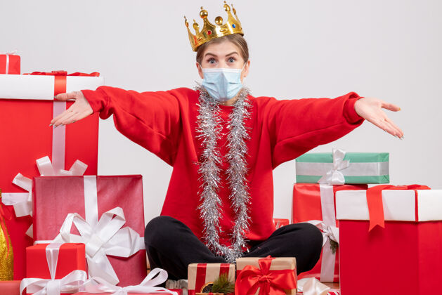 颜色正面图年轻女性戴着面具和皇冠坐在那里 手里拿着圣诞礼物面具年份礼物