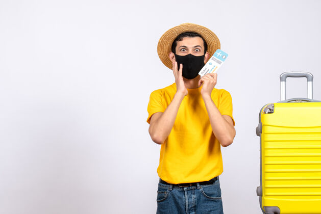 成人前视图困惑的年轻人穿着黄色t恤站在黄色手提箱旁拿着旅行票站立人黄色