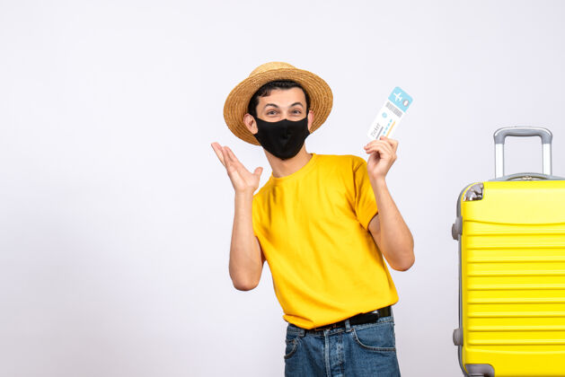 工作室正面图身着黄色t恤的快乐年轻人站在黄色手提箱旁举着旅行票视图微笑人