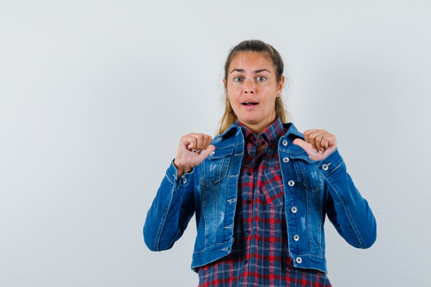 拇指年轻的女士指着自己的大拇指在衬衫 夹克衫和困惑的样子 前视图衬衫夹克女孩