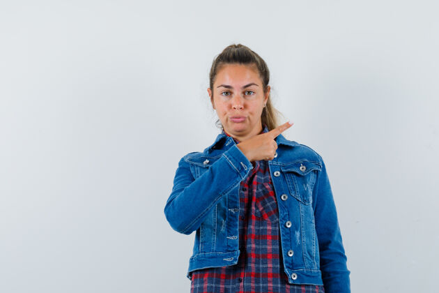 一个年轻女子指着旁边的衬衫 夹克衫和看起来自信 前视图手衬衫夹克