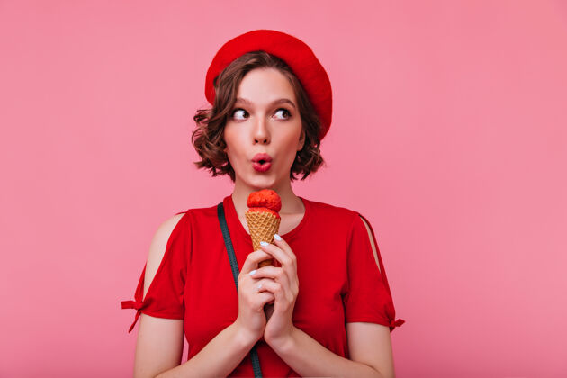 欧洲穿着迷人贝雷帽的优雅年轻女子在吃冰淇淋穿着红色套装的情绪化女孩在享受甜点粉色年轻理发