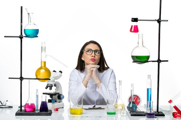 酒精前视图穿着白色医疗服的女化学家坐在那里思考着白色背景的科学病毒-实验室大流行病毒玻璃前面烧杯