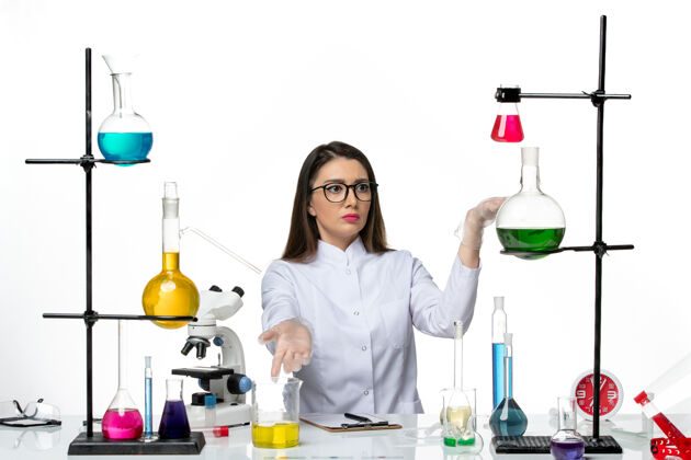 大流行前视图穿着白色医疗服的女化学家坐在白色背景上实验室病毒冠状病毒大流行科学药品实验套装