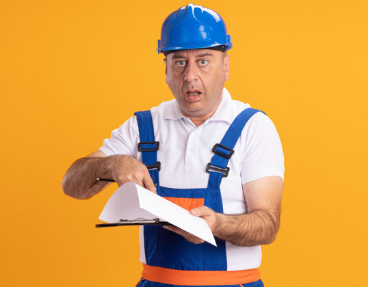 人震惊的白人成年建筑工人穿着制服拿着铅笔指着剪贴板上的橙色铅笔人制服