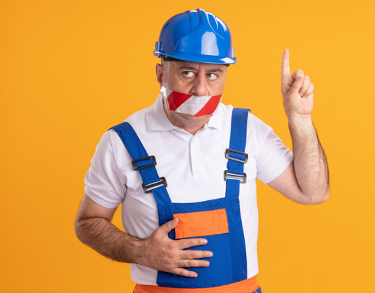 焦虑焦虑的白人成年建筑工人穿着制服 用胶带捂住嘴巴 指着橘子封面磁带人