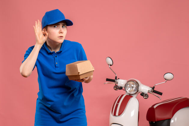 服务正面图：带着小食品包的女快递员坐在粉色的工作服上听着工作自行车工披萨女前面工作包装