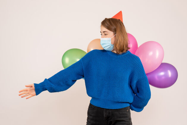 隐藏正面图：戴着无菌口罩的年轻女性把五颜六色的气球藏在背后面具背部病毒