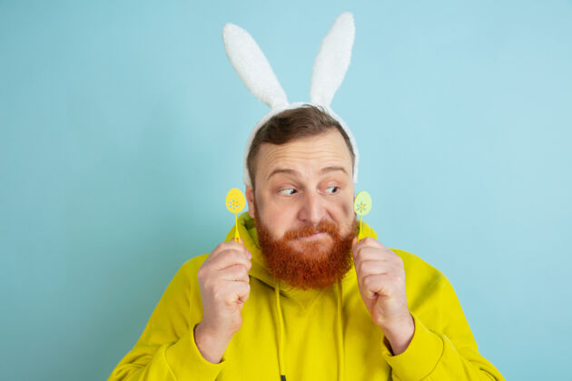 黄色白种人 传统装潢为复活节兔子 蓝色工作室背景上有明亮的休闲服情感兔子强壮