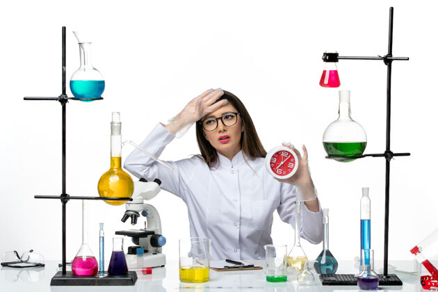 医学前视图：身穿白色医疗服的女化学家手持红色时钟站在白色背景的科学病毒冠状病毒-大流行实验室高尔夫专业时钟