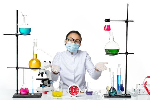 专业前视图：穿着医疗服的女化学家 戴着面罩 坐在白色背景上的溶液化学实验室病毒-喷溅化学喷溅医生