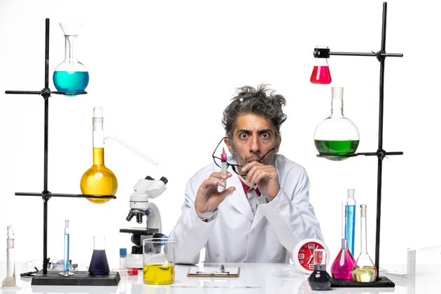实验室正面图身穿医疗服的男科学家拿着注射在白色办公桌上的化学冠状病毒-实验室病毒西装罐子专业