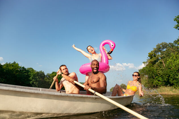 飞溅一群快乐的朋友在河里欢笑和游泳阳光明媚的日子里 穿着泳装的男女们在河边乘船欢庆夏日 友谊 度假 周末的概念周末潜水庆祝