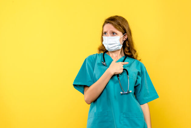 专业黄色墙上戴着无菌口罩的女医生的正视图绝育人制服
