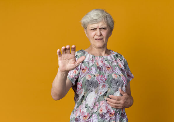 不高兴不高兴的老妇人举起手孤立在橙色的墙上老人女人手