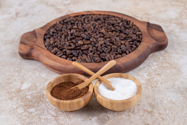 糖磨碎的咖啡和一个糖碗旁边的咖啡豆堆在一个木制托盘上芳香豆粉