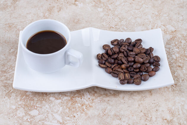 盘子一小杯咖啡旁边是一堆咖啡豆豆子咖啡