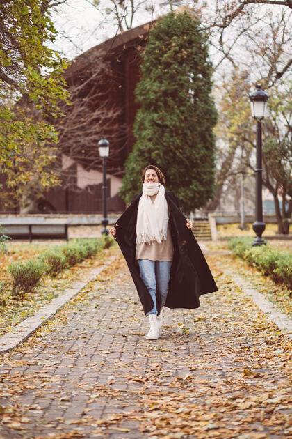 时尚公园里穿着冬天黑外套白围巾的女人的户外肖像叶子秋天女性