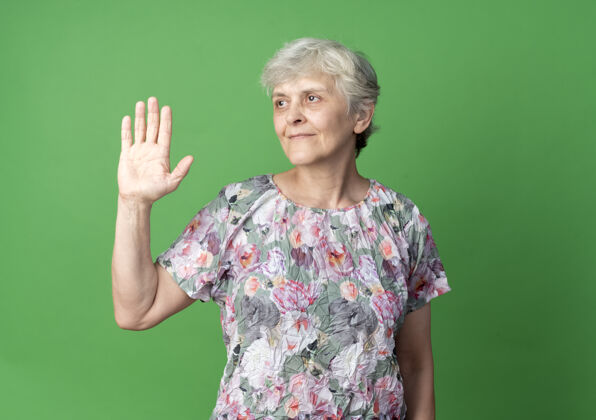 老的高兴的老妇人举手看着隔离在绿墙上的一面女人手老的
