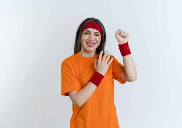 空气微笑的年轻运动女性戴着头带和腕带握紧拳头看着保持手在空气中隔离拳头保持头带