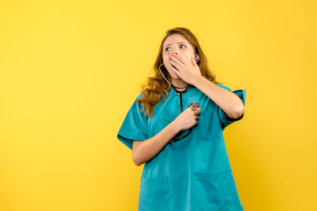黄色黄色墙上女医生使用听诊器的正面图专业成人女医生