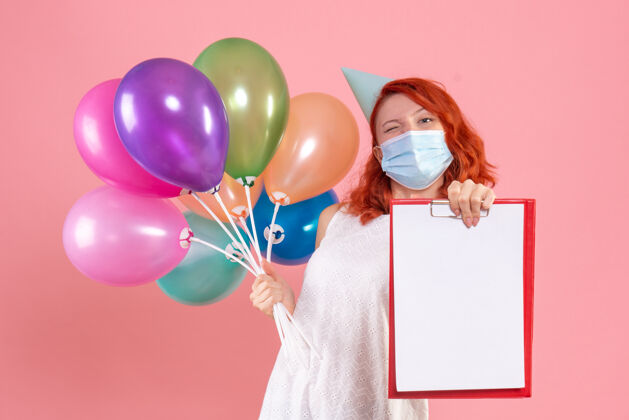 流行病正面图年轻女性手持五颜六色的气球和粉红色面具上的文件说明生日派对举行