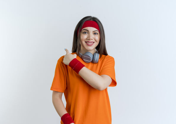 头带面带微笑的年轻运动女性戴着头带和腕带 脖子上戴着耳机 看着身后的孤立女人腕带运动